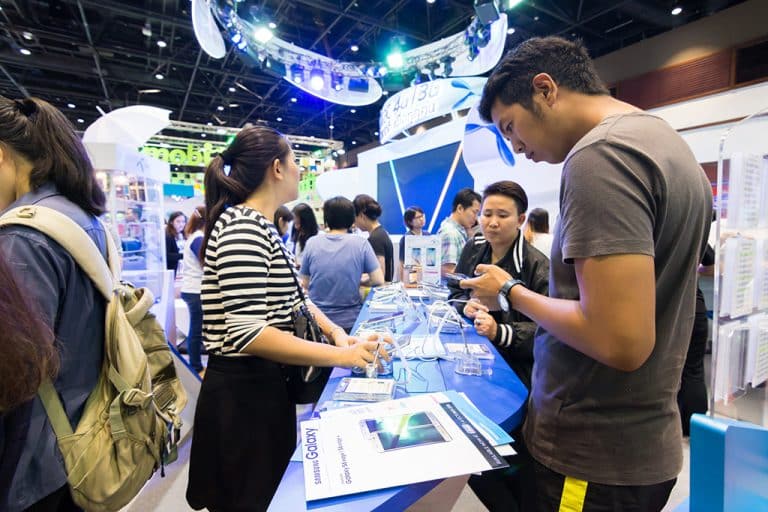 Multiple people standing around a table/booth at at trade show.